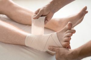 Hands of rehabilitation clinician wrapping foot and ankle of man with bandage